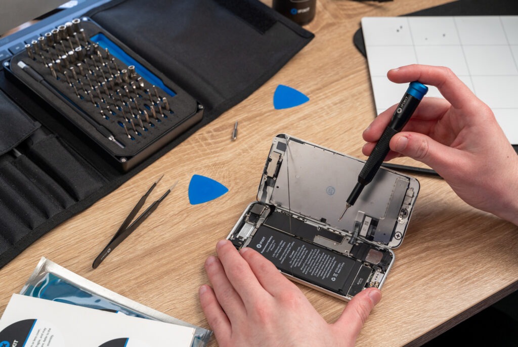 A man repairs an iPhone at home using an iFixit toolkit